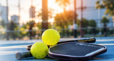 Pickleball paddle and two yellow balls on a court at sunset